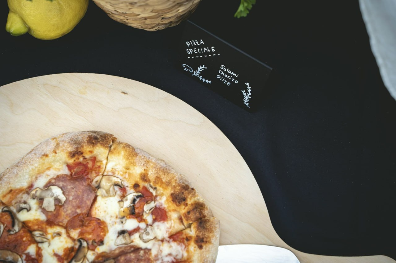Pizza Speciale mit Salami, Chorizo und Pilzen auf Holzschieber
